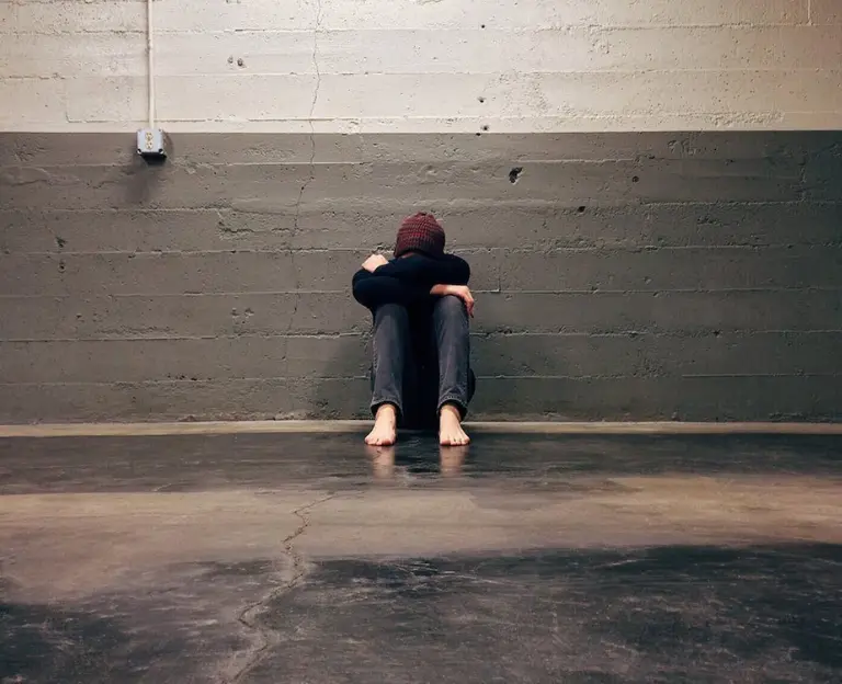 Fearful young man crouched, expressing anxiety and fear in a compelling image.